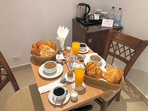 Een ontbijttafel met brood, een soepkom, een kop koffie, een glas sinaasappelsap en een waterkoker.