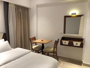 A hotel room with a bed, a desk, two chairs, a mirror, and a small table. - Maxim Hotel (Cairo)