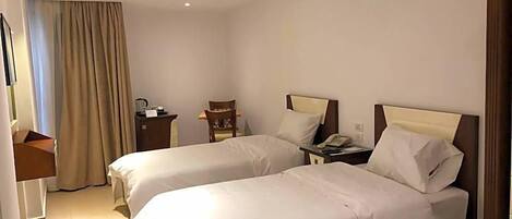A hotel room with two beds, a desk, a chair, a nightstand, and a window with curtains.