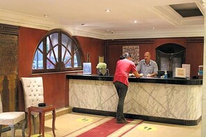 A reception desk with a marble counter, a large arched window, and a white upholstered chair. - Maxim Hotel (Cairo)