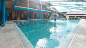 An indoor swimming pool with a slide, a covered area, and a building with multiple floors and balconies. - Alamaris Resort (Morong)