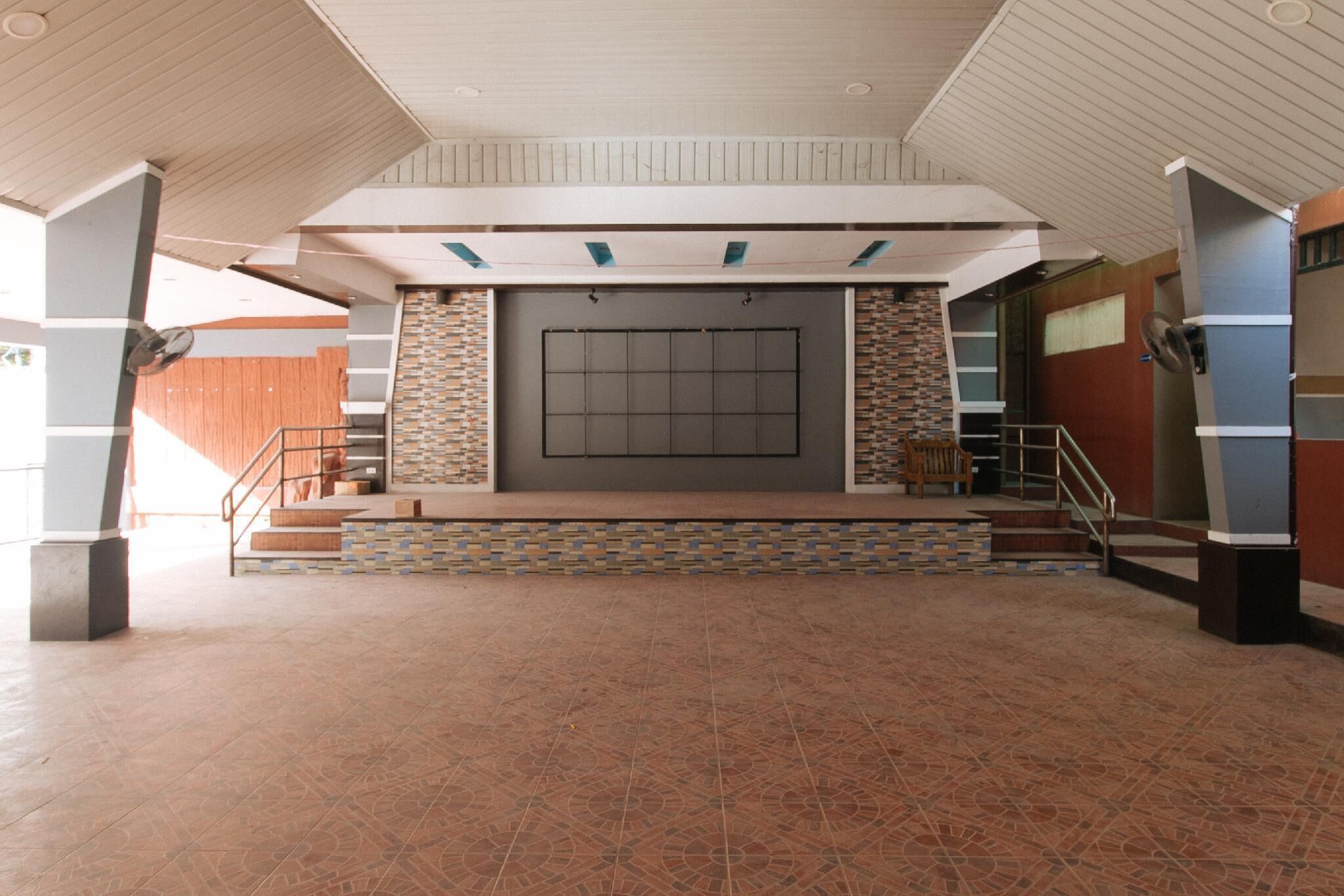 A spacious lobby with a tiled floor, a staircase with a handrail, and a large wall-mounted screen.
