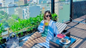 A person relaxing on a sun lounger with a city view, a glass table with a drink, and a handbag on the side. - Duke Casa Apartment (Da Nang Municipality)