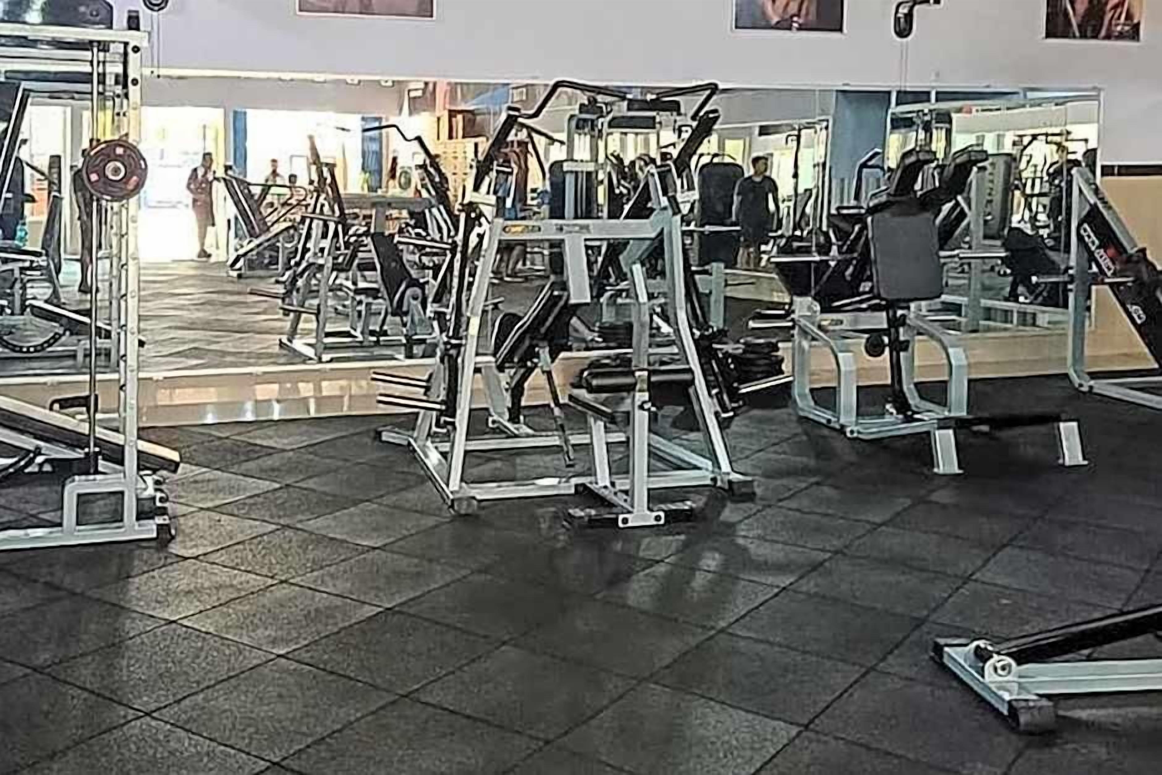 A gym with various exercise machines, a tiled floor, and a doorway leading to another room.
