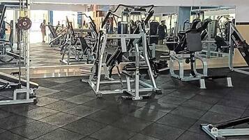 A gym with various exercise machines, a tiled floor, and a doorway leading to another room.