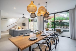 Un comedor moderno con una mesa de madera larga, sillas negras y lámparas colgantes de fibra.
