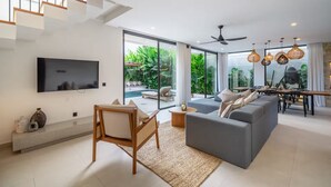 Ein modernes Wohnzimmer mit grauem Sofa, Holzstuhl, Fernseher und einem Essbereich mit Tisch und Stühlen.