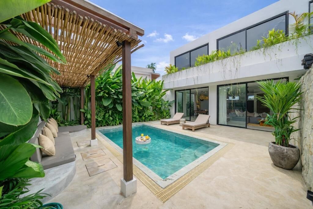 A modern outdoor pool area with a pergola, lounge chairs, and lush greenery.