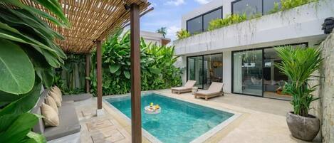 A modern outdoor pool area with a pergola, lounge chairs, and lush greenery.