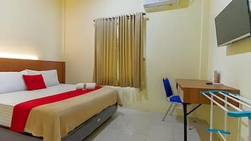 A hotel room with a bed, a desk, a chair, an air conditioning unit, a television, and a window with curtains.