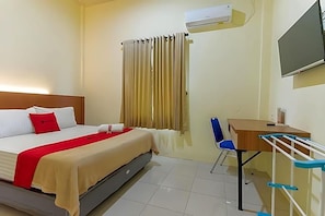 A hotel room with a bed, a desk, a chair, an air conditioning unit, a television, and a window with curtains. - Reddoorz Syariah Near Transmart Jambi 2 (Jambi)