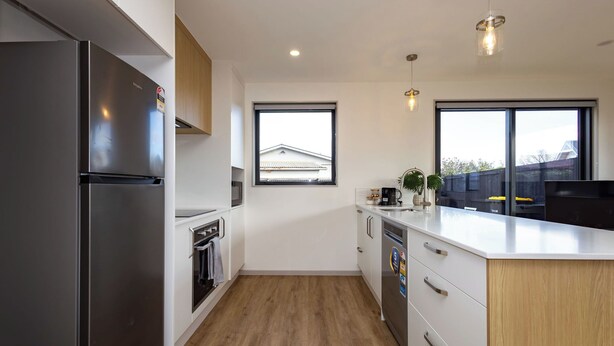 Una cocina moderna con refrigerador de acero inoxidable, armarios blancos, piso de madera y un ventanal grande.