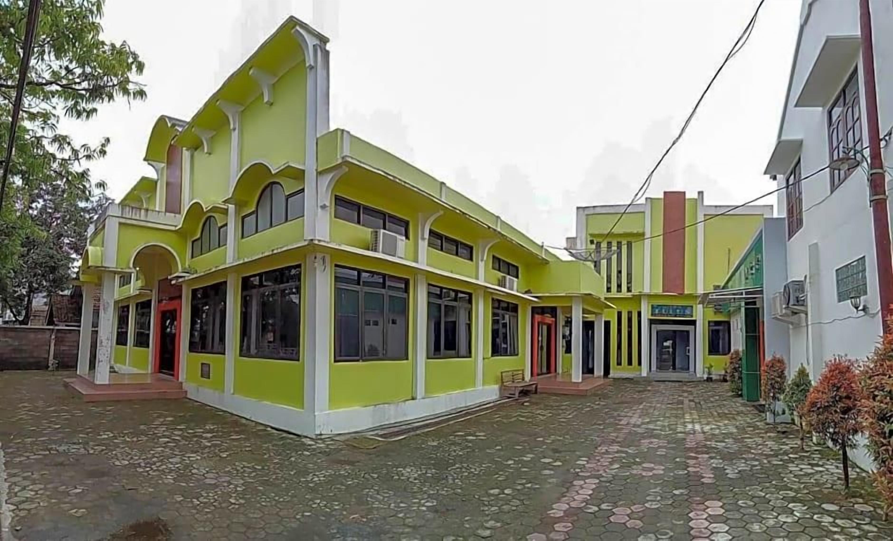 A multi-story building with a green facade, large windows, and a paved courtyard.