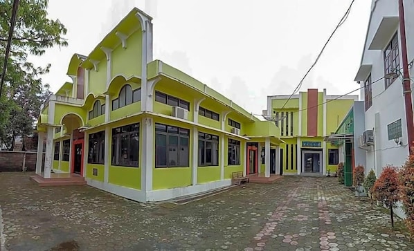 A multi-story building with a green facade, large windows, and a paved courtyard.