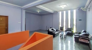 Um quarto amplo com uma grande janela, um sofá, uma mesa de centro e uma porta.
