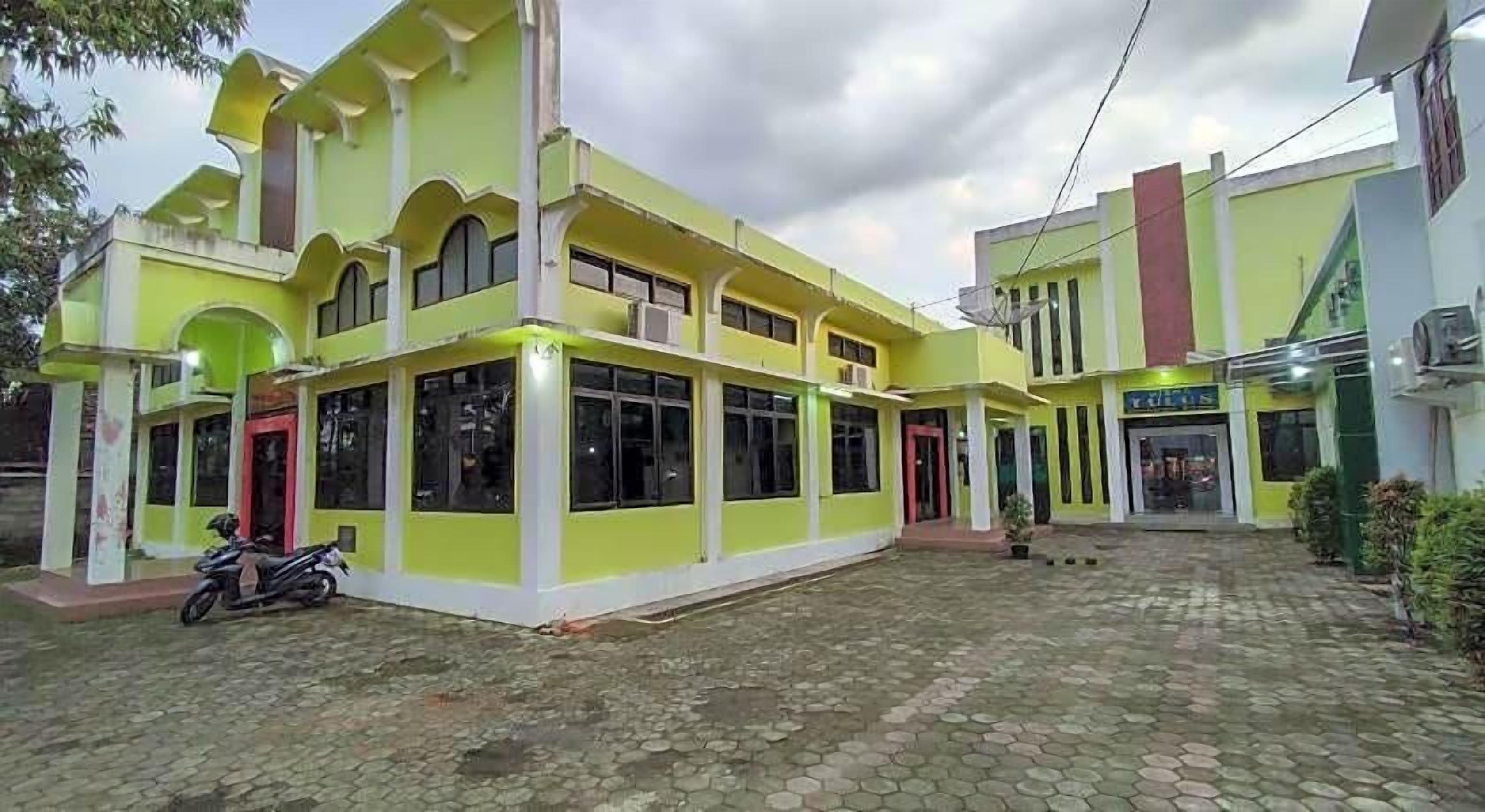 A two-story building with a green facade, large windows, and a paved courtyard.