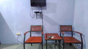A room with two wooden chairs, a small table, and a television mounted on the wall.