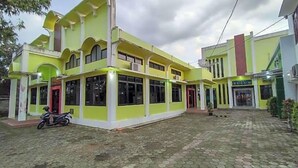 A two-story building with a green facade, large windows, and a paved courtyard.