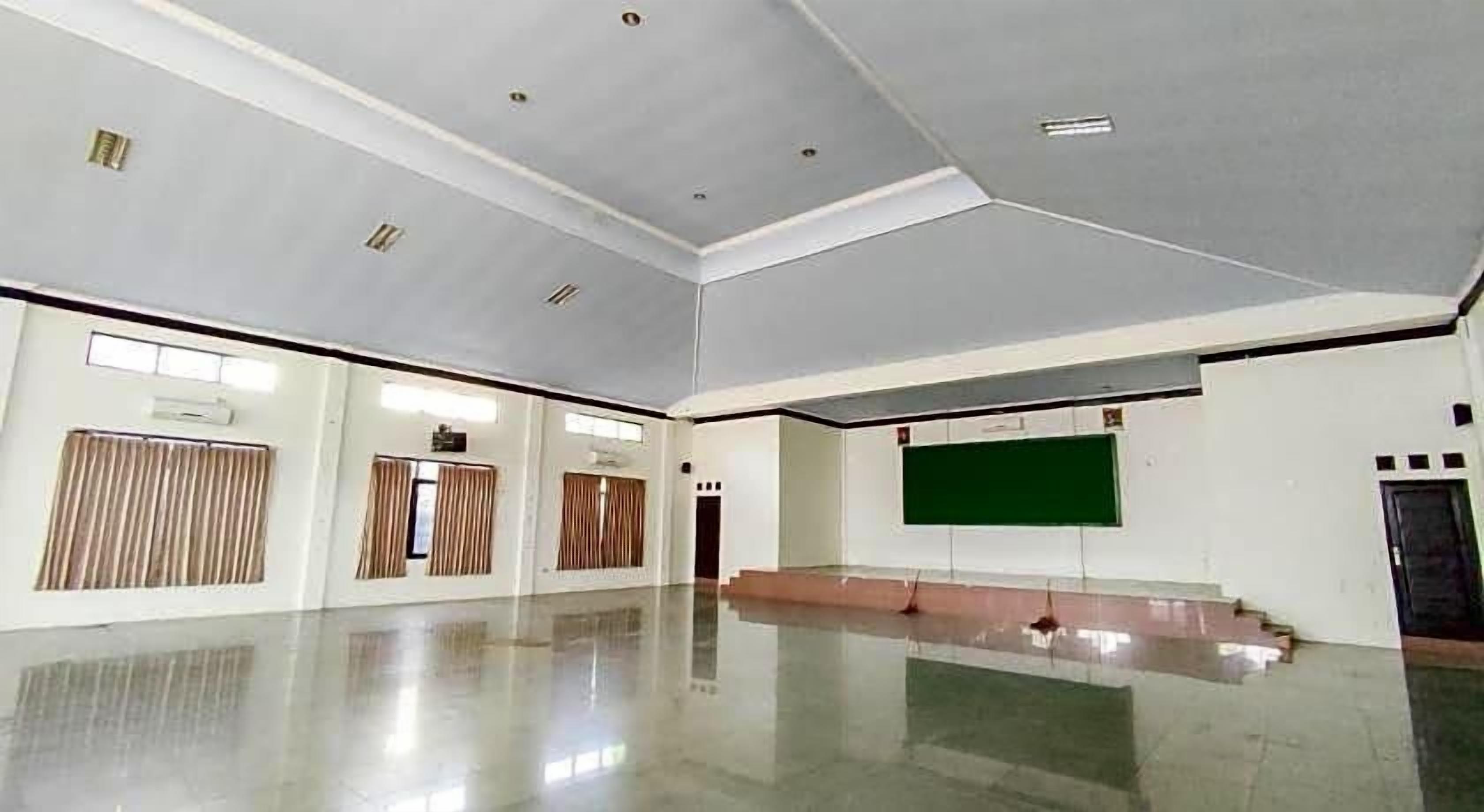 A spacious room with a polished floor, a large green screen, and a stage area.