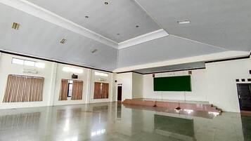 A spacious room with a polished floor, a large green screen, and a stage area.