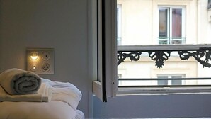 Une chambre d’hôtel avec un lit, une fenêtre donnant sur un balcon et une prise électrique au mur.