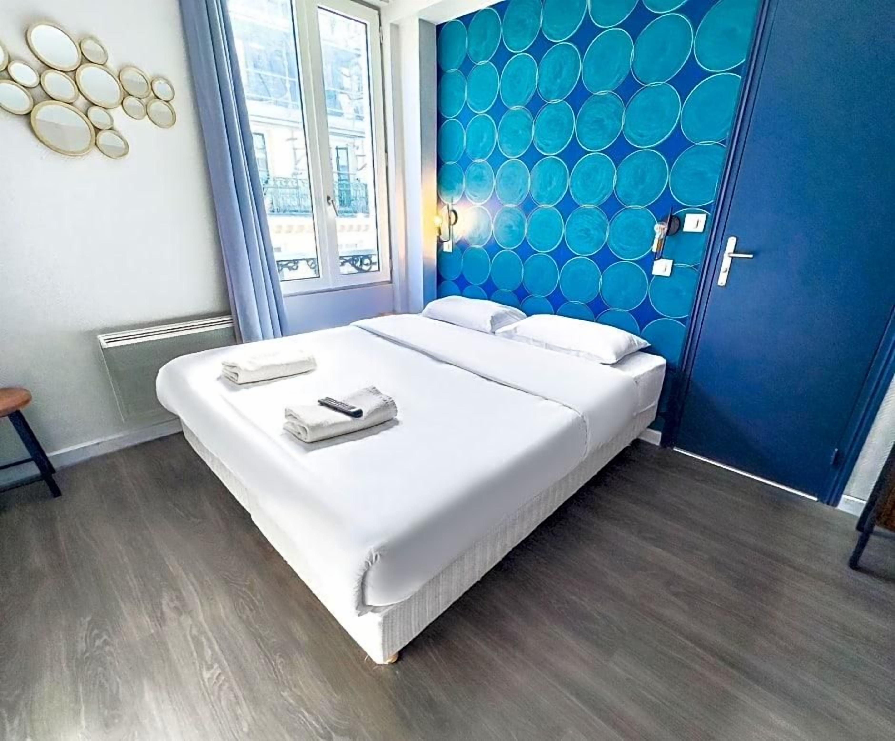 A hotel room with a bed, a blue wall with circular patterns, a window, and a door.