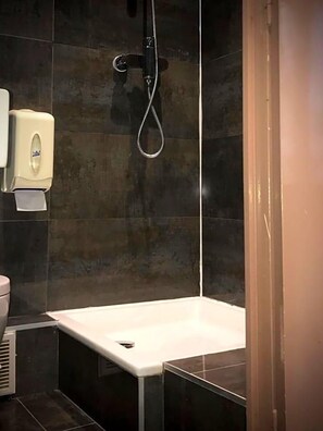 A bathroom with a white bathtub, a handheld showerhead, and a soap dispenser on the wall. - Plug Inn Montmartre By Hiphophostels (Paris)