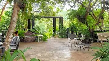 An outdoor seating area with tables and chairs, surrounded by lush greenery and trees.