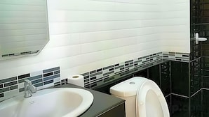 Un baño con un lavabo blanco, un espejo, un inodoro y un salpicadero de azulejos negros.