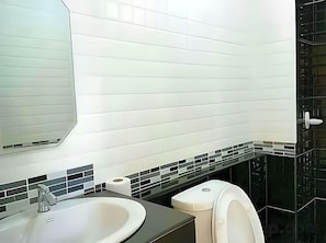 Ein Badezimmer mit weißem Waschbecken, einem Spiegel, einer Toilette und einer schwarzen, gefliesten Rückwand.