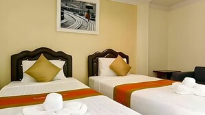 Habitación de hotel con dos camas, cada una con cabecera, almohadas y manta. Hay un cuadro en la pared y una mesita con una silla.