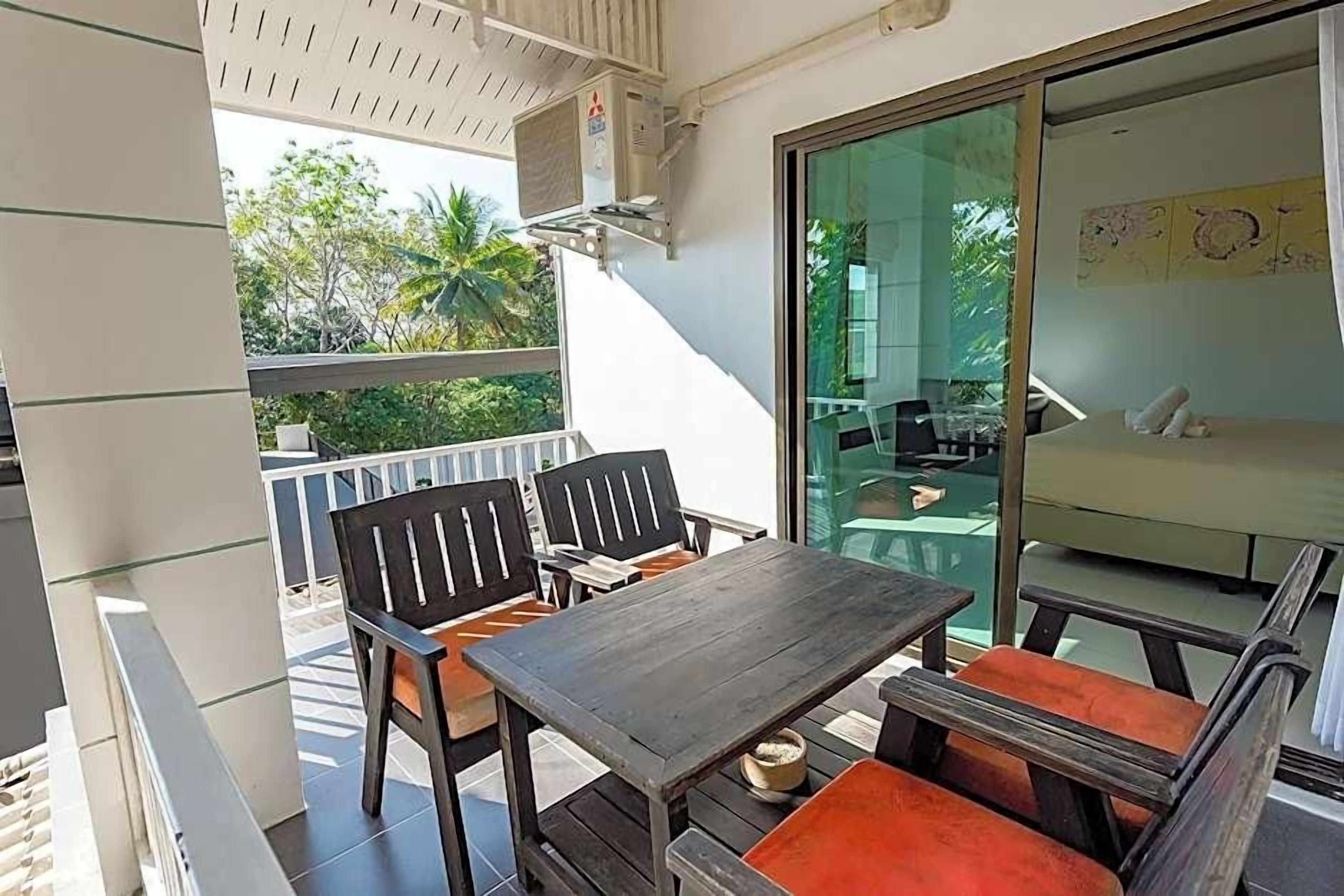 A balcony with a table and chairs, a sliding glass door leading to a room, and an air conditioning unit.