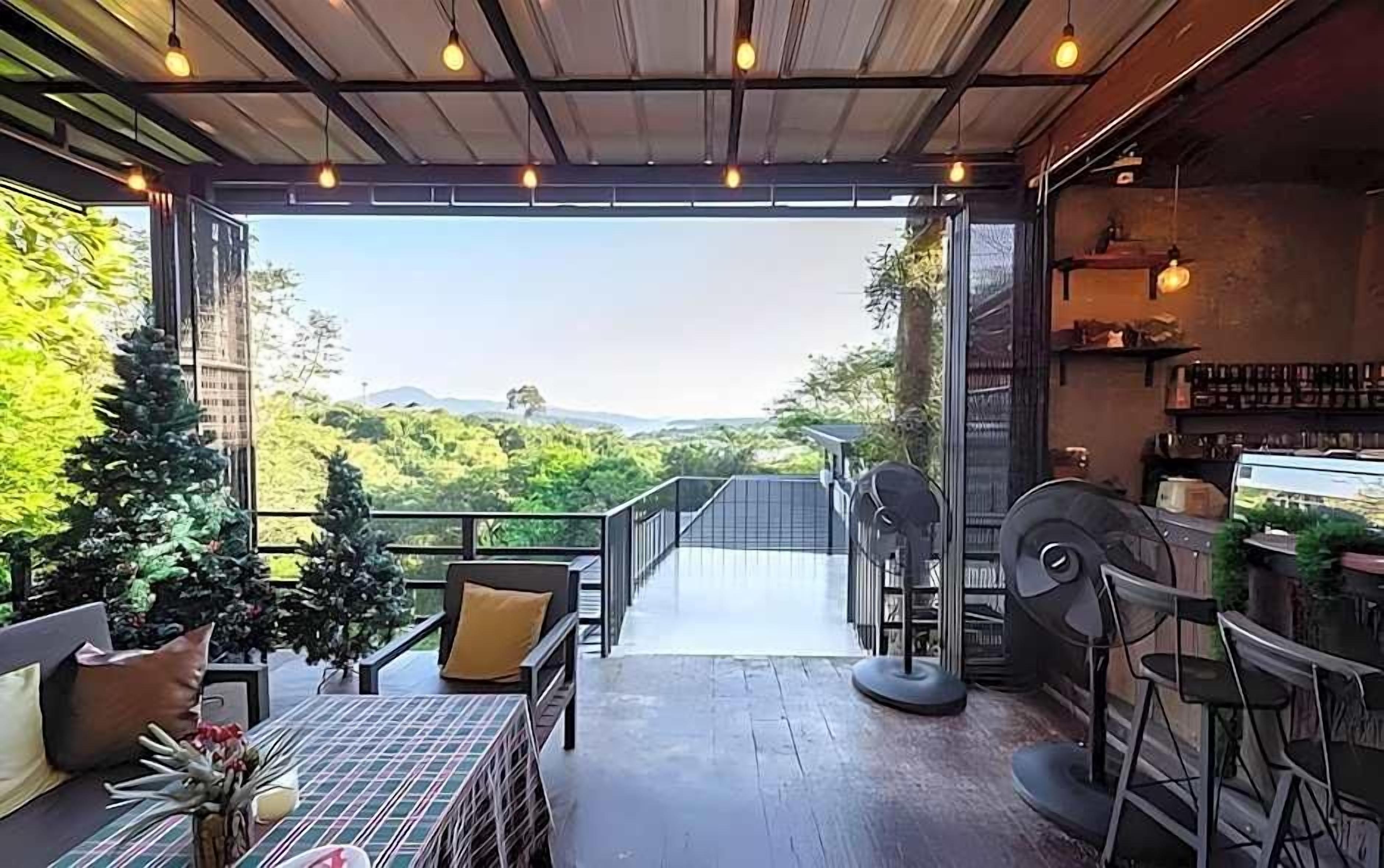 An open-air patio with a view of greenery and hills, furnished with chairs and a table, and a bar area with stools.