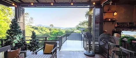 An open-air patio with a view of greenery and hills, furnished with chairs and a table, and a bar area with stools.