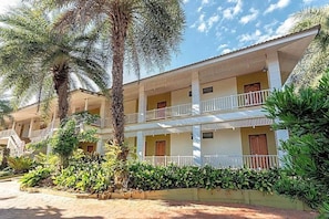 Un edificio de varios pisos con balcones, rodeado de plantas tropicales.