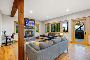 A modern living room with a stone fireplace, a large gray sofa, and a television mounted on the wall. - Majestic Mtn Views Hot Tub Sauna Arcade Room (Penrose)
