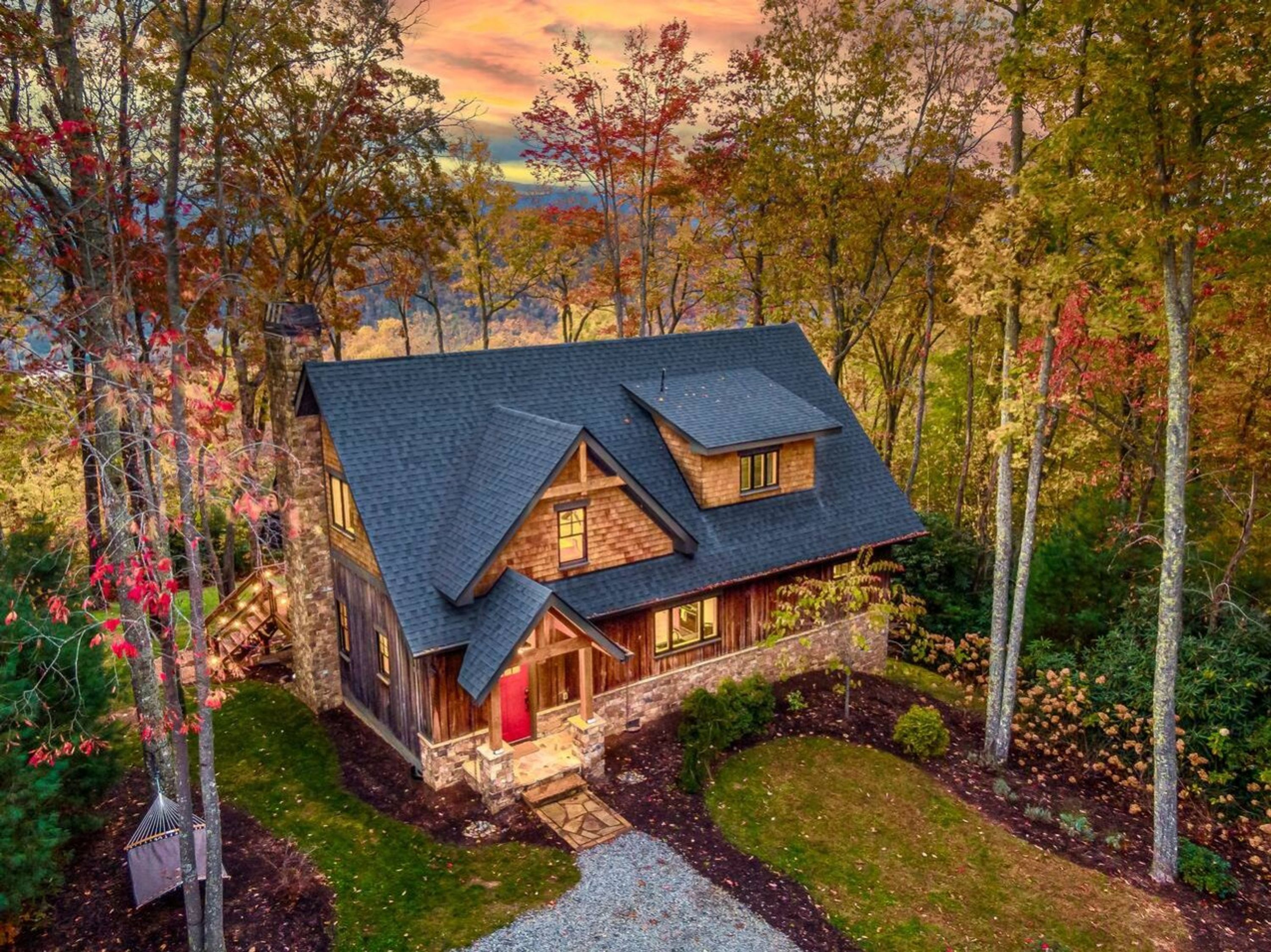 A two-story log cabin with a stone foundation, a steeply pitched roof, and a red door.