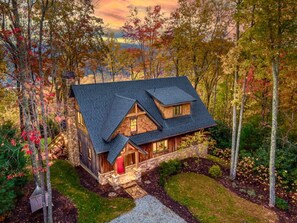 A two-story log cabin with a stone foundation, a steeply pitched roof, and a red door. - Majestic Mtn Views Hot Tub Sauna Arcade Room (Penrose)