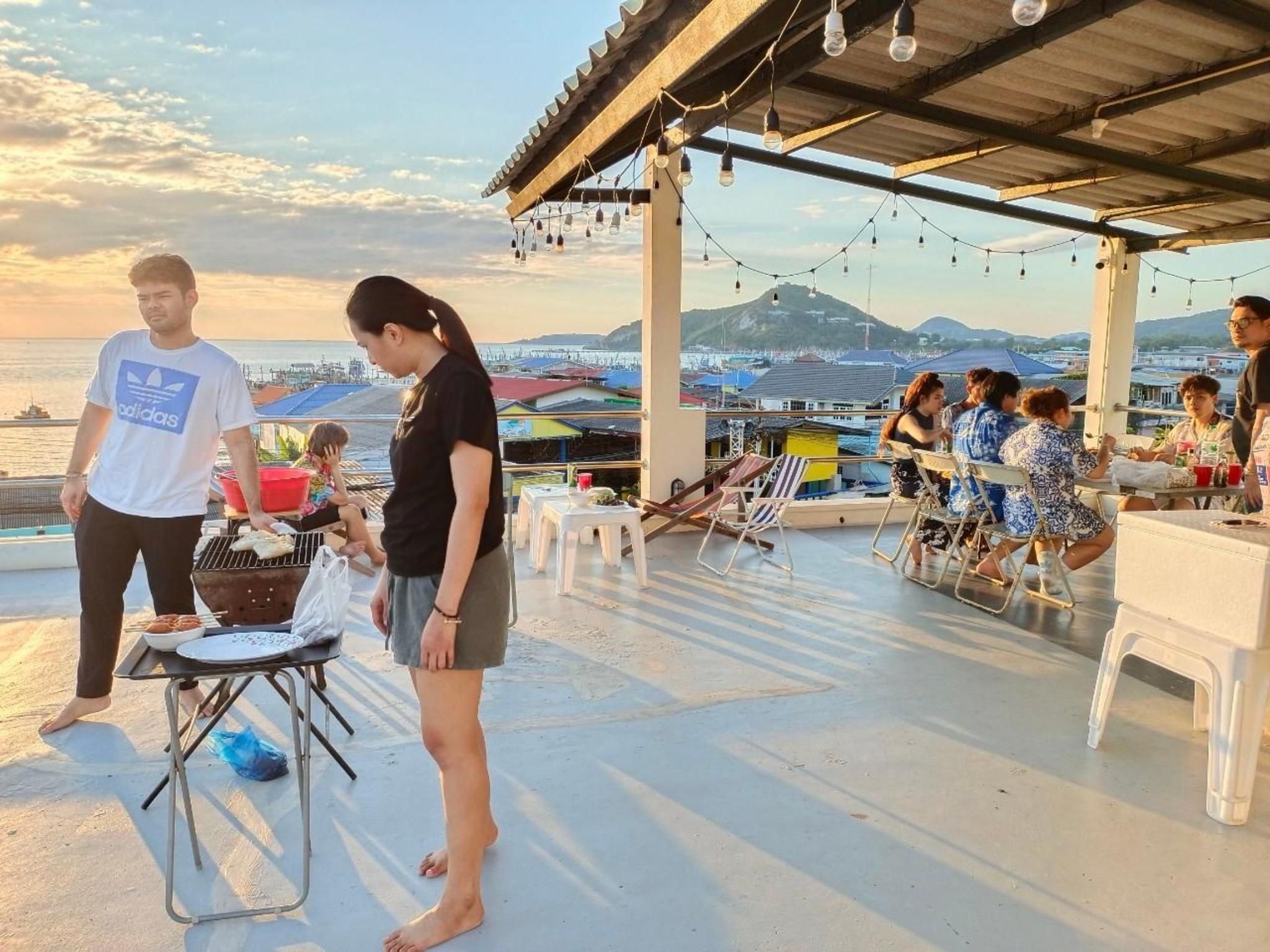 An outdoor dining area with tables and chairs, a grill, and a view of the sea and mountains.