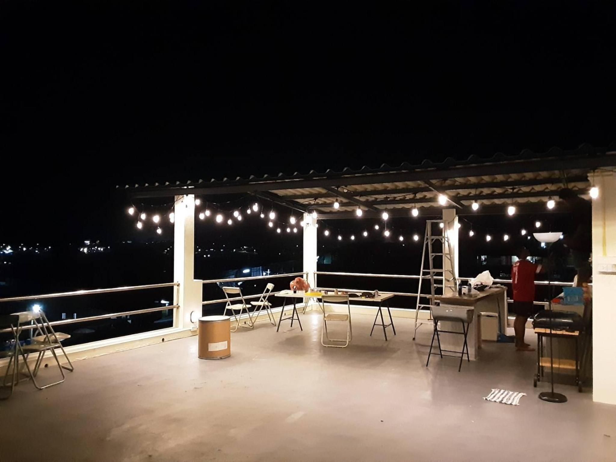 An outdoor patio with string lights, chairs, tables, and a ladder.