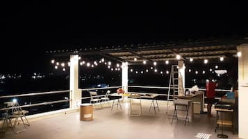 An outdoor patio with string lights, chairs, tables, and a ladder.