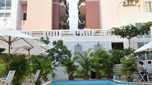 A swimming pool with lounge chairs and potted plants, surrounded by multi-story buildings with balconies. - Hung Vuong Hotel (Tuy Hoa)