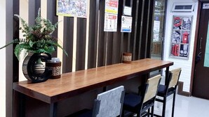 A reception desk with a wooden top and black metal chairs. There are informational posters on the wall behind the desk. - Great House99 (Bangkok)