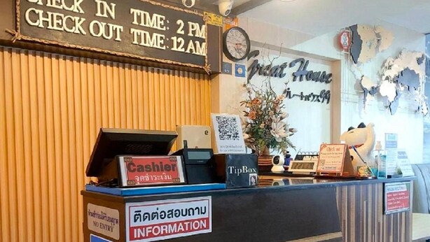 A reception desk with a sign indicating check-in time and a clock. - Great House99 (Bangkok)
