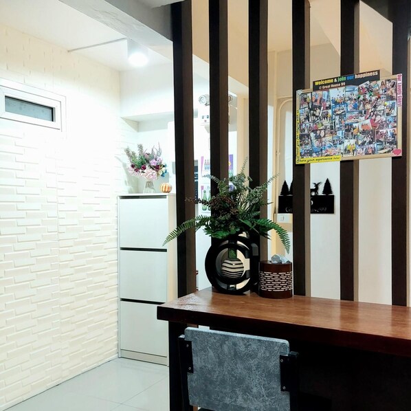A hotel reception area with a wooden reception desk, a chair, a wall-mounted photo collage, and a potted plant. - Great House99 (Bangkok)