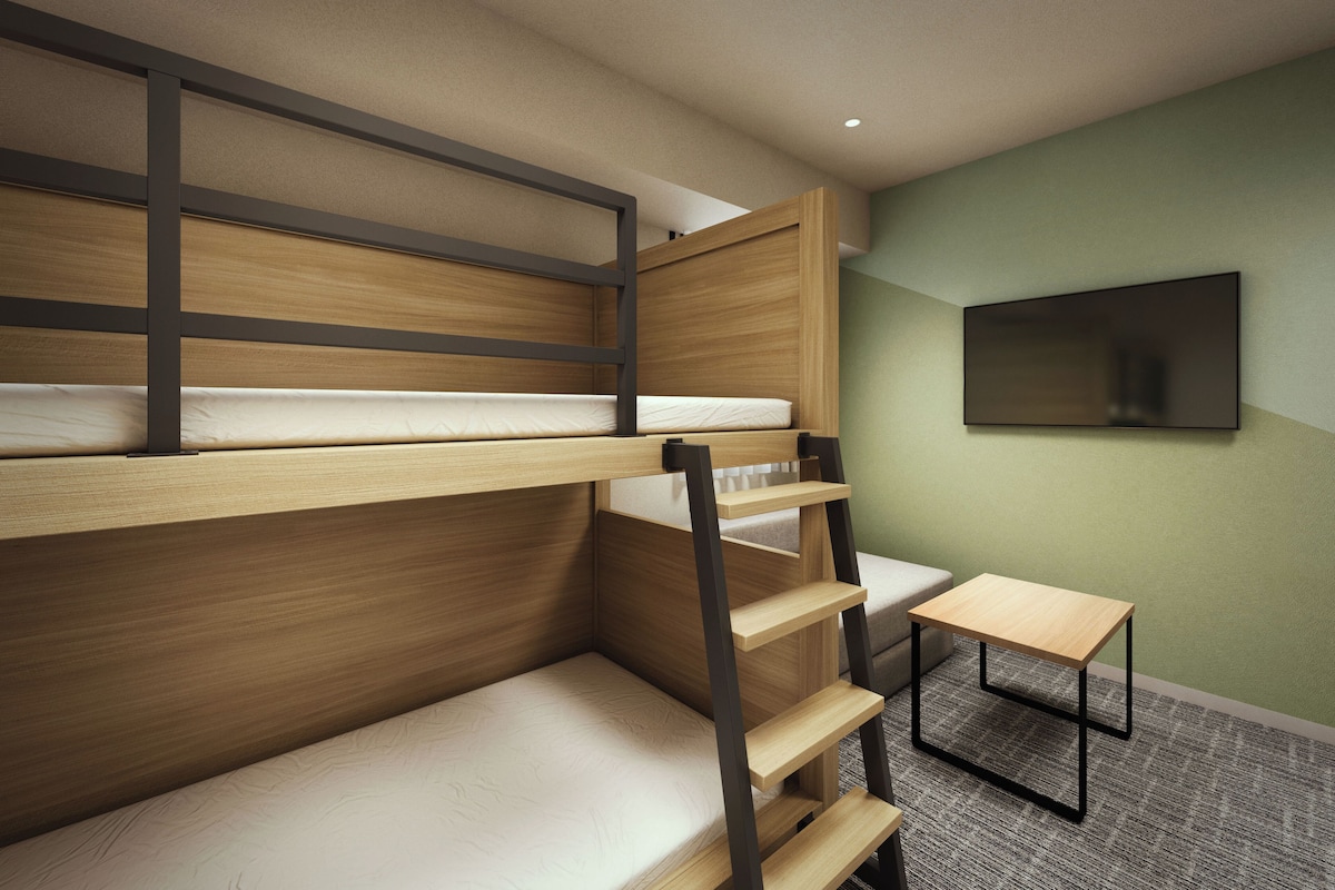 Ein Stockbett mit an der Wand befestigtem Fernseher, ein kleiner Tisch und ein Teppichboden.