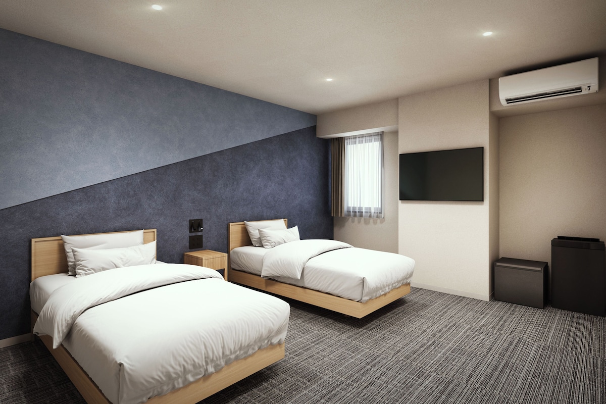 Ein modernes Hotelzimmer mit zwei Betten, einem Flachbildfernseher, einer Klimaanlage und einem Fenster mit durchsichtigen Vorhängen.