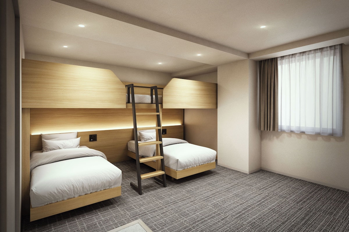 Ein Hotelzimmer mit Etagenbetten, einer Leiter und einem Fenster mit Vorhängen.