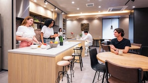 A modern kitchen with a central island, bar stools, and a dining area with a round table and chairs. - GRAND HOSTEL LDK Hiroshima (Hiroshima)