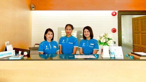 Un comptoir d’accueil avec trois employés en uniforme bleu, un arrangement floral blanc et une porte en bois en arrière-plan.